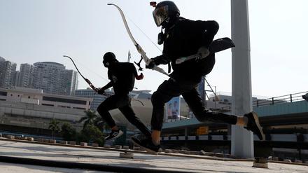 Mit Pfeil und Bogen bewaffnete Demonstranten laufen durch Hongkong.