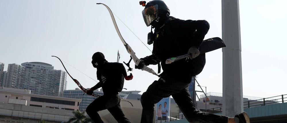 Mit Pfeil und Bogen bewaffnete Demonstranten laufen durch Hongkong.