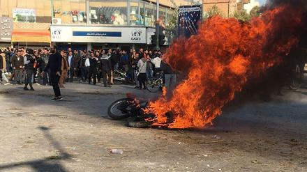 Iranische Demonstrant*innen versammeln sich um ein brennendes Motorrad bei einem Protest gegen die Erhöhung von Benzinpreisen. 