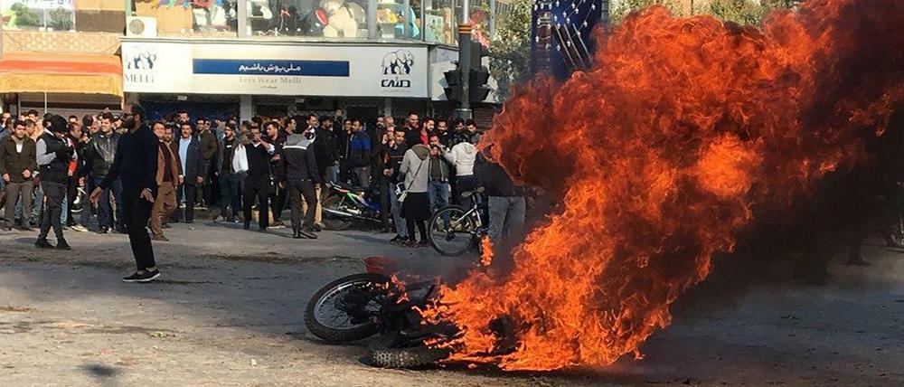Iranische Demonstrant*innen versammeln sich um ein brennendes Motorrad bei einem Protest gegen die Erhöhung von Benzinpreisen.