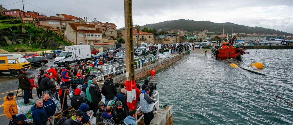 Einwohner der Gemeinde Aldan beobachten einen Einsatz, bei dem zwei Schlepper ein Drogen-U-Boot aus dem Wasser ziehen.