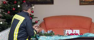 Ein Feuerwehrmann zündet während einer Vorführung in einem nachgebauten Wohnzimmer Kerzen an einem Adventskranz an.