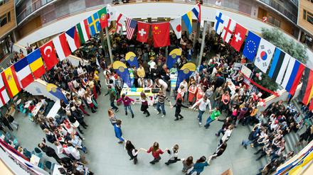 Studierende tanzen unter internationalen Flaggen in einem Hochschulauditorium.