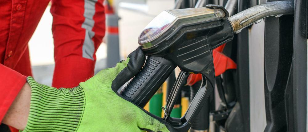 Ein Tankwart nimmt eine Zapfpistole aus der Halterung einer Zapfsäule einer Tankstelle.