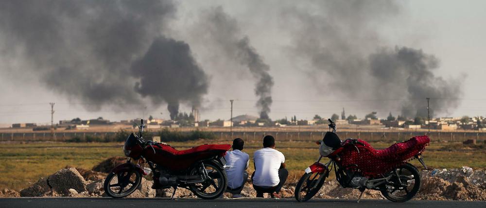Zwei Männer blicken an der nordsyrischen Grenze auf aufsteigenden Rauch.