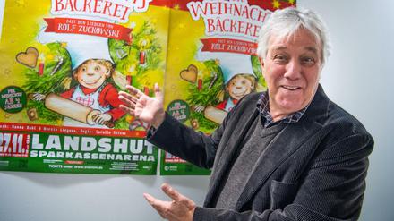 Rolf Zuckowski vor einem Poster seines Musicals „Die Weihnachtsbäckerei“ 