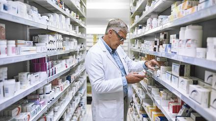 Ein Apotheker begutachtet Medikamente in einem Regal.