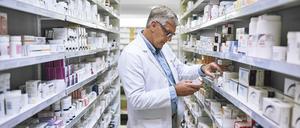 Ein Apotheker begutachtet Medikamente in einem Regal.