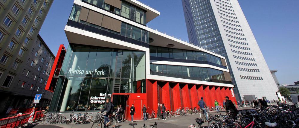 Passanten und Fahrräder vor einem avantgardistischen Neubau auf dem Campus der Universität Leipzig.