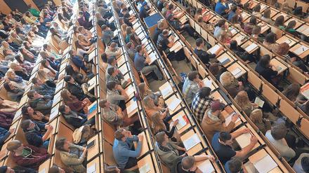 Studierende sitzen in einem Hörsaal, einige Plätze sind frei geblieben.