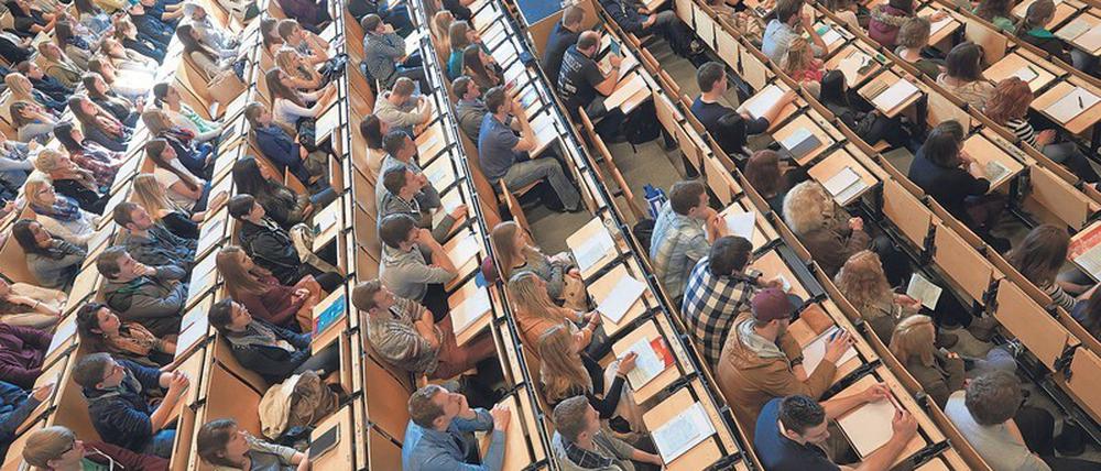 Studierende sitzen in einem Hörsaal, einige Plätze sind frei geblieben.