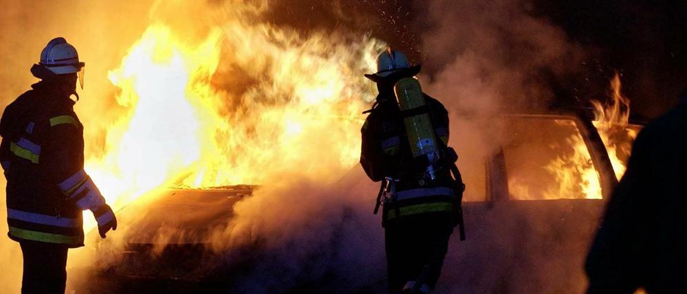 Feuerwehrmänner löschen ein brennendes Auto - Symbolbild.