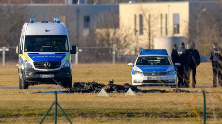 Flugzeugabsturz in Strausberg: Zwischen zwei Fahrzeugen der Polizei sind die verkohlten Reste eines Kleinflugzeuges zu sehen.