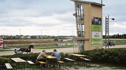 Kulisse aus einer anderen Zeit. Zur Trabrennbahn Karlshorst gehört ein sandiger Rundkurs, ein wackliger Zielturm, eine Fressbude aus Holz und eine Tribüne.