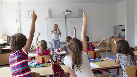 Eine Lehrerin steht vor einer Klasse, in der sich alle Kinder melden.