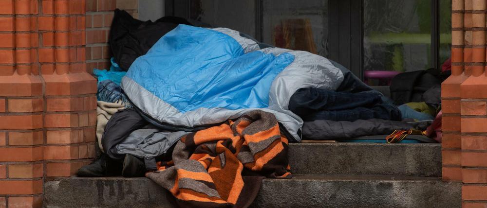 Ein Obdachloser liegt unter einer Decke in einem Eingang einer Kirche in Kreuzberg.