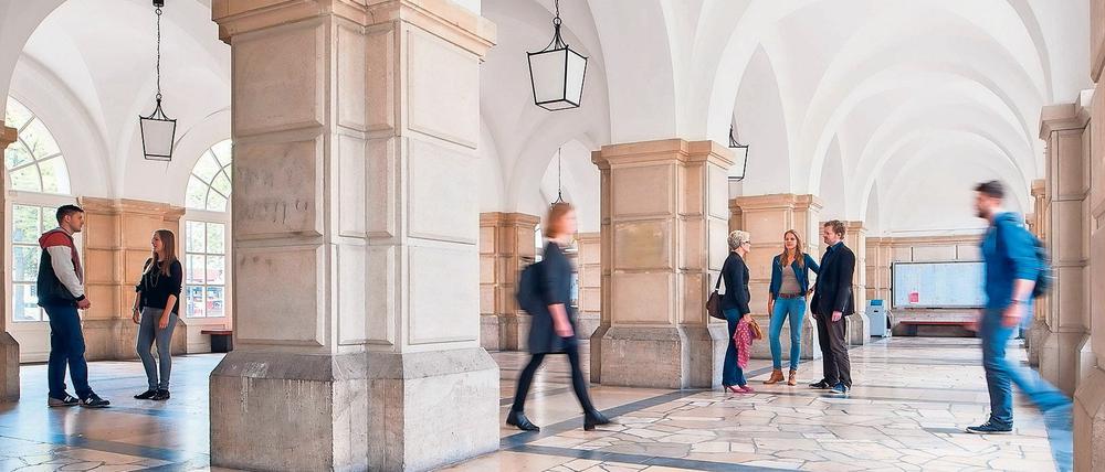 Studierende stehen und gehen im Foyer eines Hochschulgebäudes.