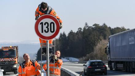 Straßenwärter montieren an einer Autobahn ein Schild.