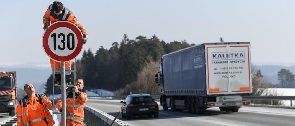 Straßenwärter montieren an einer Autobahn ein Schild.