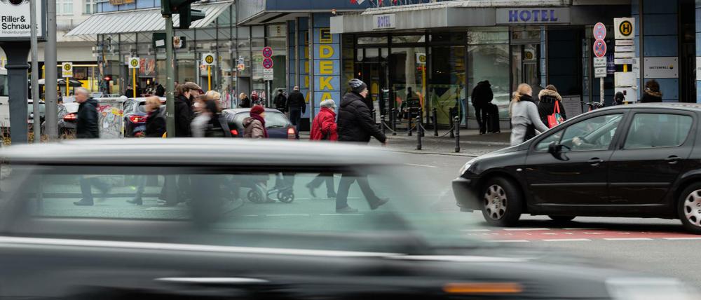 Ein Auto fährt schnell über die Kreuzung Schloßstraße / Grunewaldstraße in Steglitz, im Hintergrund weitere Autos und Fußgänger.