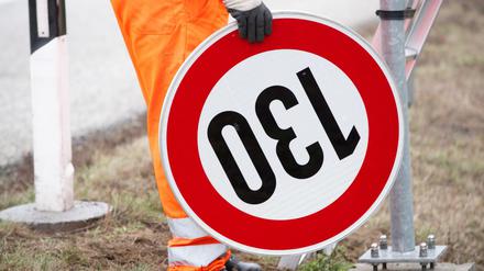 Ein Straßenwärter hält an der Autobahn A24 ein Verkehrsschild mit der Geschwindigkeitsangabe 130 Stundenkilometer.