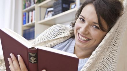 Junge Frau liest in der Hängematte ein Buch.