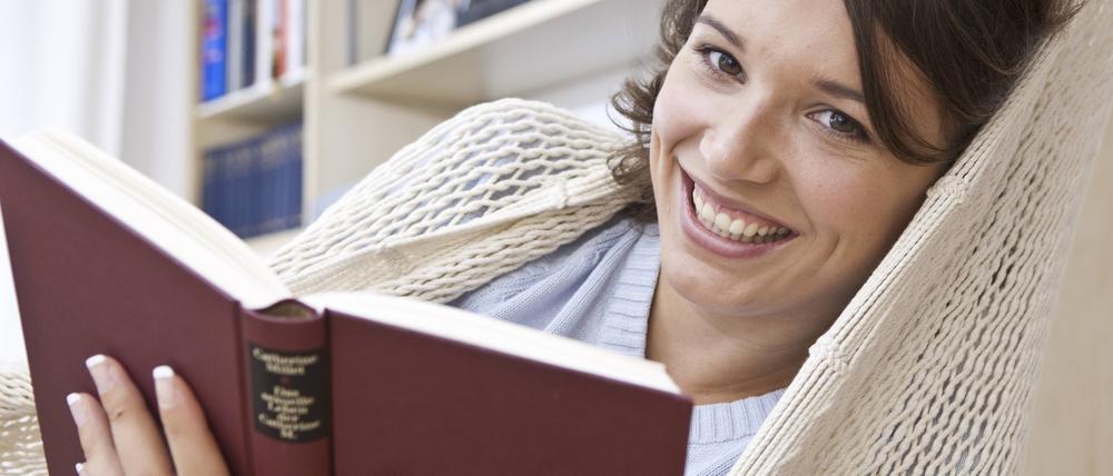 Junge Frau liest in der Hängematte ein Buch.