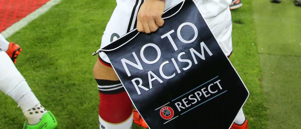 Viel Symbolik, aber immer wieder Ärger. Ein deutscher Nationalsspieler hält einen Wimpel mit der Aufschrift "No to Racism" beim Einlaufen in der Hand. 