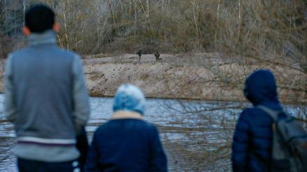 Migranten stehen am Fluss Mariza auf türkischer Seite, während ihnen auf der griechischen Seite Soldaten gegenüber stehen.