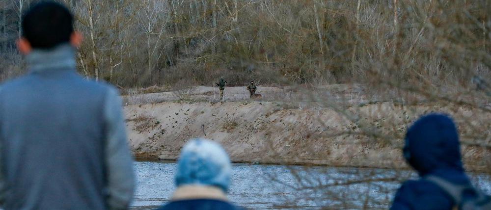 Migranten stehen am Fluss Mariza auf türkischer Seite, während ihnen auf der griechischen Seite Soldaten gegenüber stehen.