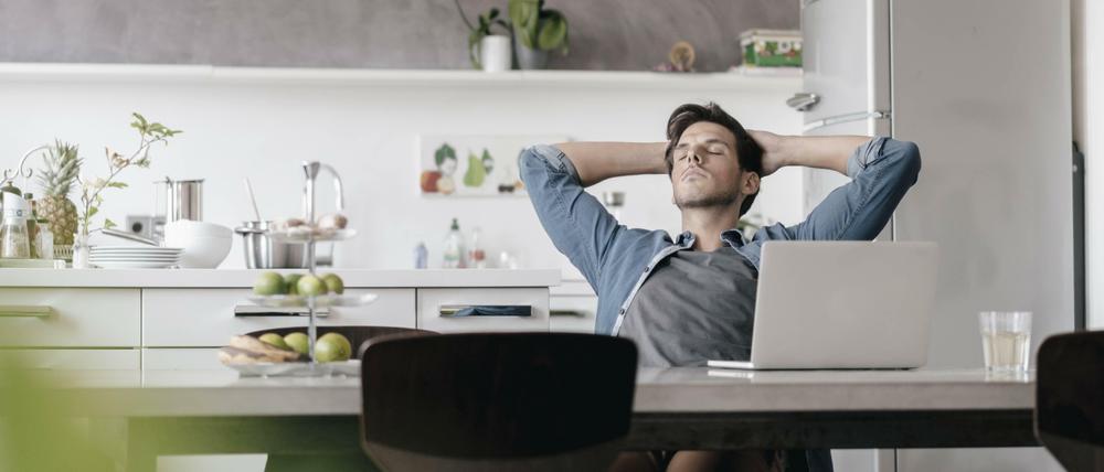 Junger Mann chillt vor Laptop in einer Küche.