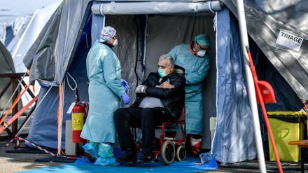 Medizinische Mitarbeiter in Schutzanzügen stehen mit einem Patienten in einem Notfallzelt in Brescia.