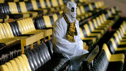 Ein als Geist verkleideter Mann sitzt auf den leeren Rängen eines Fußballstadions