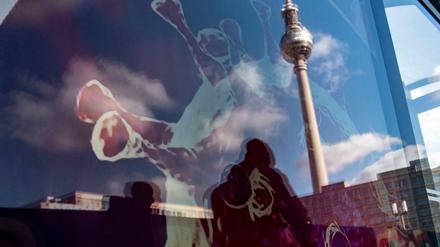 Der Fernsehturm spiegelt sich in einer Werbetafel, auf der die Zeichnung eines Coronavirus zu sehen ist.