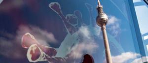 Der Fernsehturm spiegelt sich in einer Werbetafel, auf der die Zeichnung eines Coronavirus zu sehen ist.