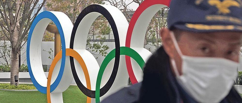 Die Spiele und das Virus. Ein Sicherheitsbeamter geht in der Nähe des neuen Nationalstadions in Tokio an den Olympischen Ringen vorbei.
