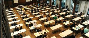 Schüler sitzen bei einer Abiturprüfung in einer historischen Aula an Einzeltischen.