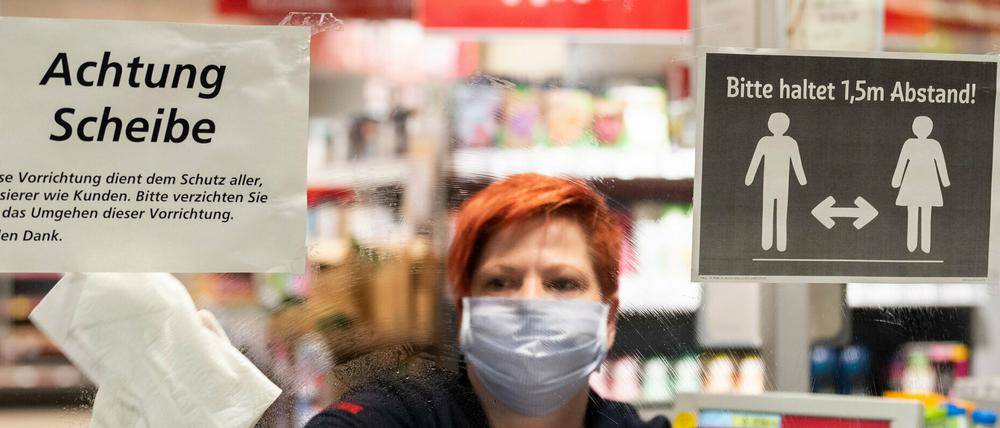 Ein Mitarbeiterin in einem Supermarkt in Dresden putzt vor Ladenöffnung eine Plexiglasscheibe, einen sogenannten "Spuckschutz", an der Kasse.
