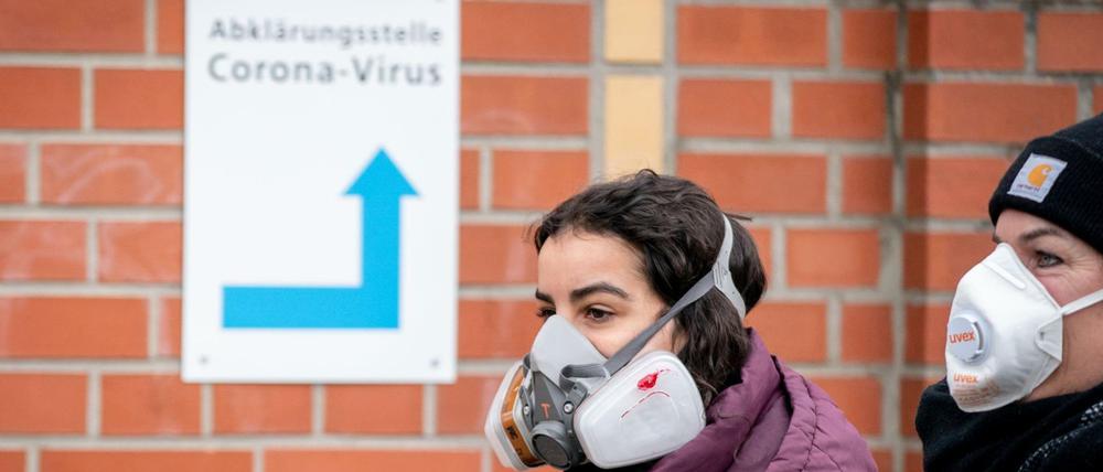 Mutter und Tochter gehen vor einem Berliner Klinikum mit Mundschutz an einem Hinweisschild vorbei.