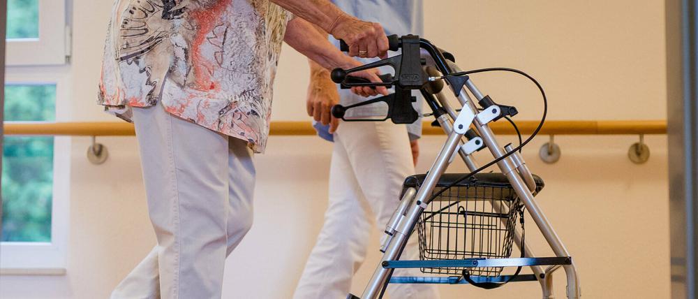 Eine Pflegekraft geht in einem Pflegeheim mit einer älteren Dame über einen Korridor.