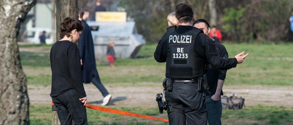 Ein Polizist spricht im Mauerpark Menschen an. Die Menschen sollen nicht im Park sitzen bleiben, um Gruppenbildungen zu vermeiden.