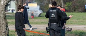 Ein Polizist spricht im Mauerpark Menschen an. Die Menschen sollen nicht im Park sitzen bleiben, um Gruppenbildungen zu vermeiden. 