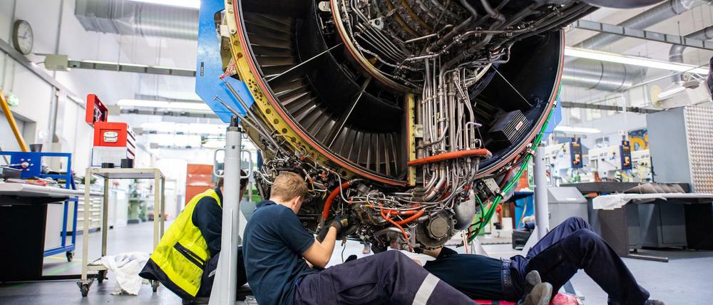 Kurzarbeit. Drei Männer arbeiten in einer Werkstatt von Lufthansa Technik am Triebwerk eines Flugzeuges. 