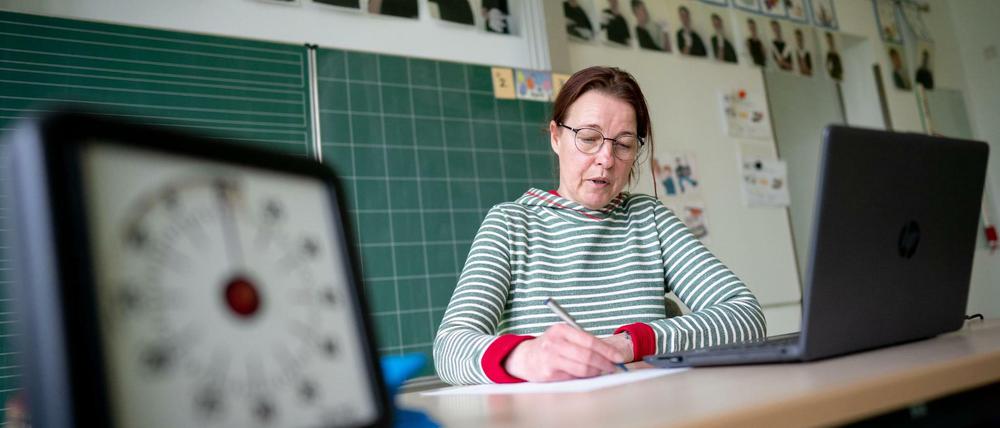 Eine Grundschullehrerin sitzt vor ihrem Laptop in einem leeren Klassenzimmer.