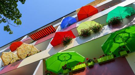  Bunte Sonnenschirme leuchten in der Mittagssonne auf Balkonen eines Mehrfamilienhauses. 