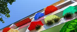  Bunte Sonnenschirme leuchten in der Mittagssonne auf Balkonen eines Mehrfamilienhauses. 