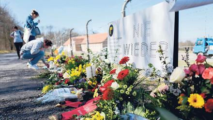 Junge Frauen stehen am Zaun der KZ-Gedenkstätte Buchenwald vor dort abgelegten Blumengebinden.