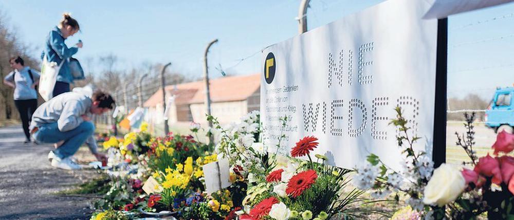 Junge Frauen stehen am Zaun der KZ-Gedenkstätte Buchenwald vor dort abgelegten Blumengebinden.