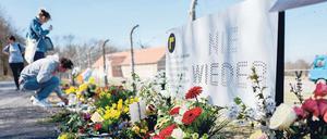 Junge Frauen stehen am Zaun der KZ-Gedenkstätte Buchenwald vor dort abgelegten Blumengebinden.