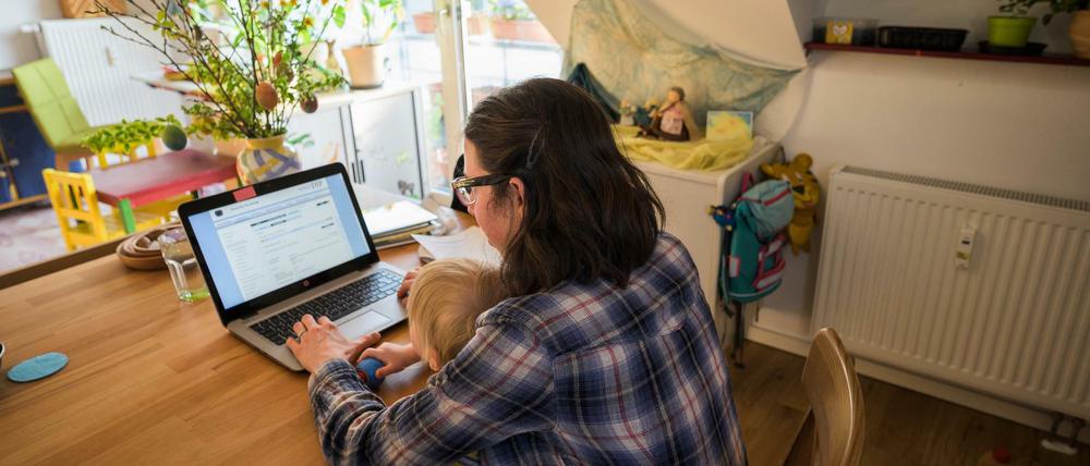 Eine alleinerziehende Mutter sitzt mit ihrem Kleinkind auf dem Schoß am Computer.